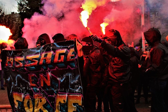 Les manifestant•es du bloc derrière une banderole "Passage en Force". Un•e manifestant•e brandit un fumigène rouge