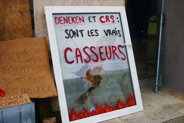 Fenêtre brisée trouvée dans une poubelle utilisée comme pancarte devant le blocage et indiquant "Deneken et les CRS sont les vrais casseurs"