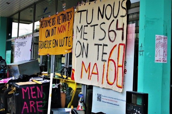 Le blocus devant l'Institut Le Bel avec des banderoles indiquant "Tu nous mets 64, on te re-Mai 68", "Réforme des Retraites on dit non. Jeunesse en lutte" et "Étudiant•es en grève". Sur une poubelle posée devant le blocus on peut lire "Men are"