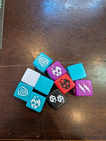 A picture of ten custom dice on the table of various colors from Uprising: Curse of the Last Emperor.