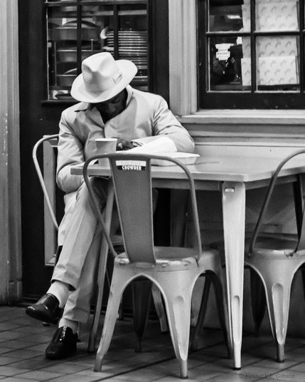 Black and white photo of a man wearing all white sitting at a table.