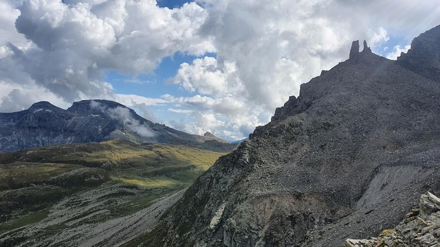 Foto einer Berglandschaft südlich vom Passo di Cornera: Im Vordergrund ein Gipfel mit zwei felsigen Türmen, im Hintergrund eine Ebene, dahinter zwei stumpfe Gipfel.