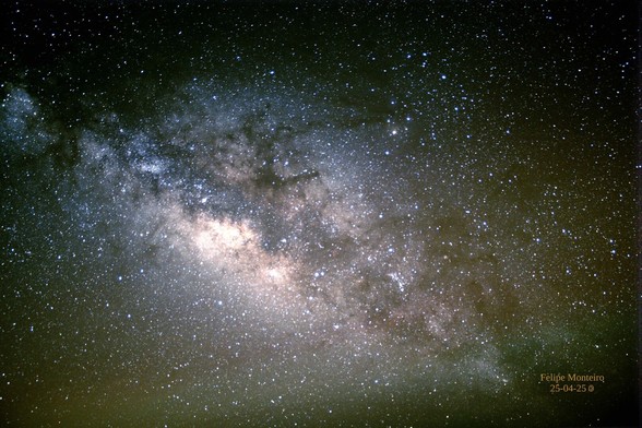Astrofotografia: o centro da Via Láctea encontra-se um pouco fora de eixo, para esquerda. A imagem mostra um campo estrelado, com um braço escuro na diagonal decrescente, e um miolo mais claro, coberto por nuvens marrons do braço da galáxia.