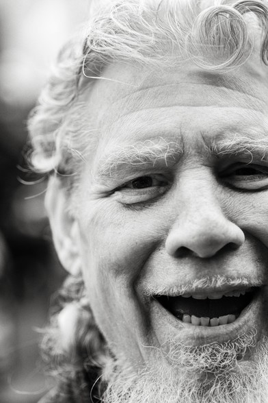 Black and white photo of a man with white hair and beard laughing.