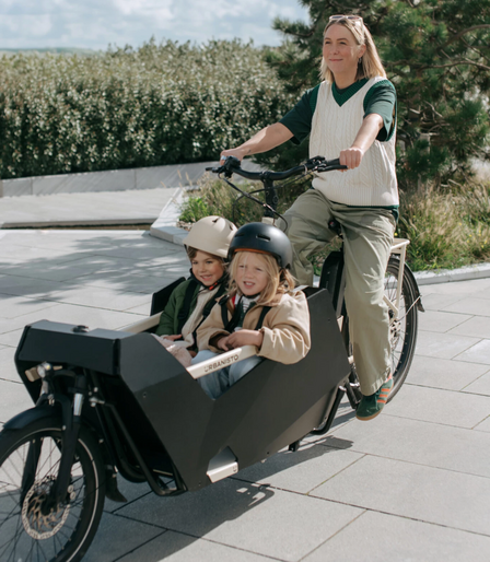Woman riding same ebike as other picture but with a cargo basket carrying two kids