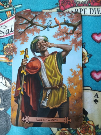 Card from the Modern Spellcaster's Tarot deck. 
Page of Wands.
A young Black man in robes and wearing a turban, leaning on a staff (wand) listening to two birds singing in a tree above.