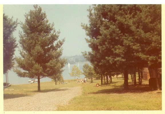 Color image of a path to a lake in Northeast Ohio, Carroll County, USA. Image shows pine trees along a path to a sandy beach, with a lake beyond with docks, swimmers, picnickers and sailboats, taken in July, 1963.