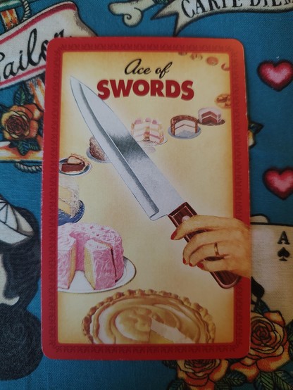 Card from Housewives Tarot deck. 
Ace of Swords. 
A hand holds a kitchen knife, with a row of cakes and pies to be cut.