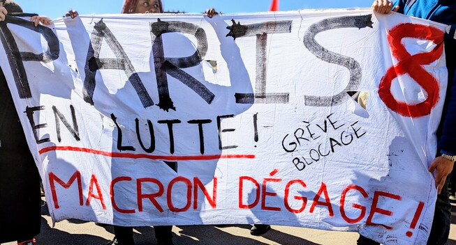 Banderole en blanc, noir et rouge. On lit "Paris 8 en lutte ! Grève blocage, Macron dégage !"