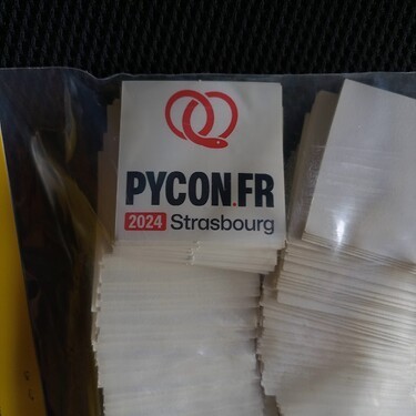 stickers pour la PyConFR 2024 à Strasbourg, fond blanc avec un logo sur le haut représentant un serpent rouge enroulé comme un bretzel, en-dessous se trouve les informations "PyConFR - 2024 Strasbourg"