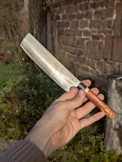 Le couteau en acier vg10 damassé tenu en main devant un mur de pierre.