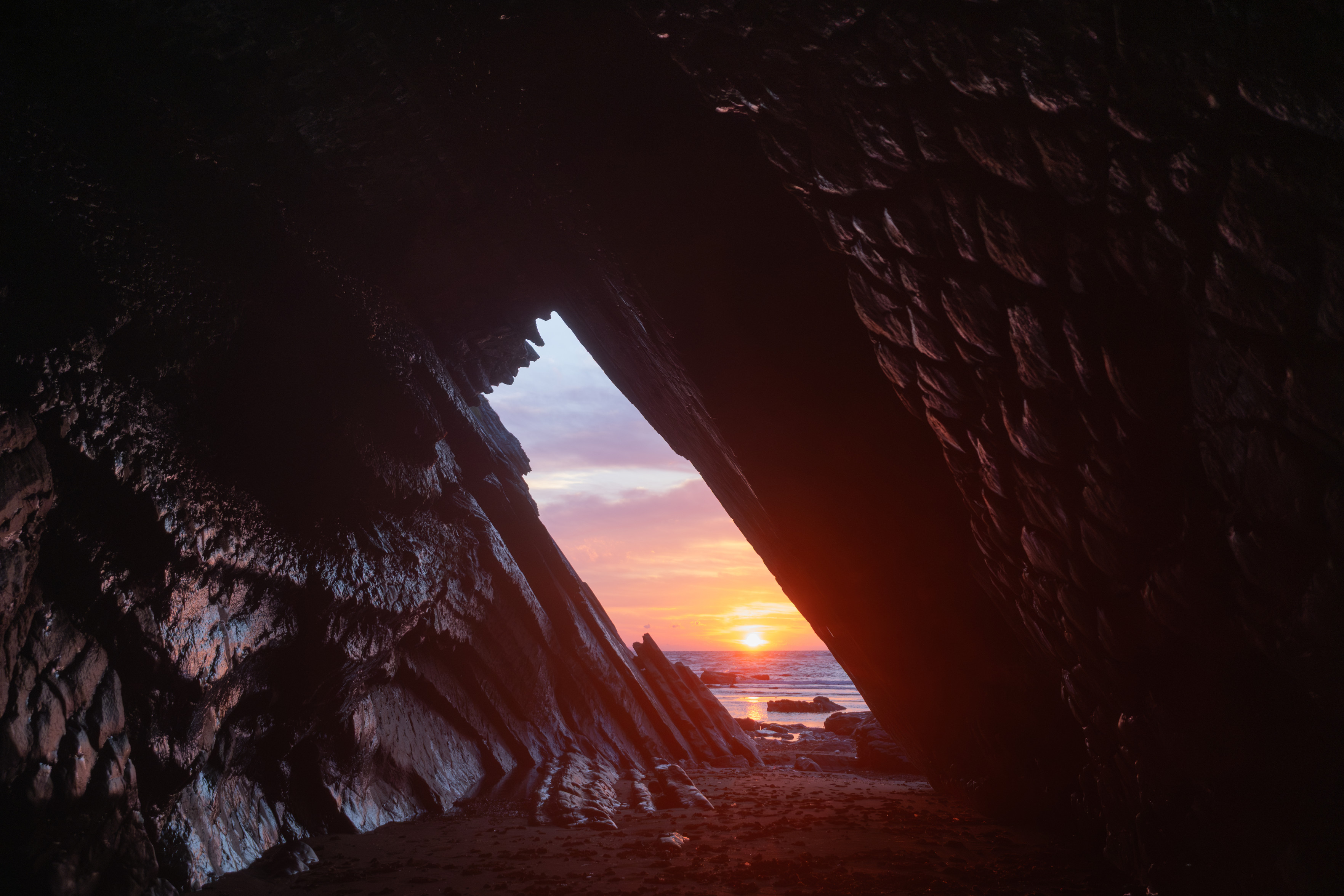 Photo prise à l'intérieur d'une grotte à marée basse durant un coucher de soleil.