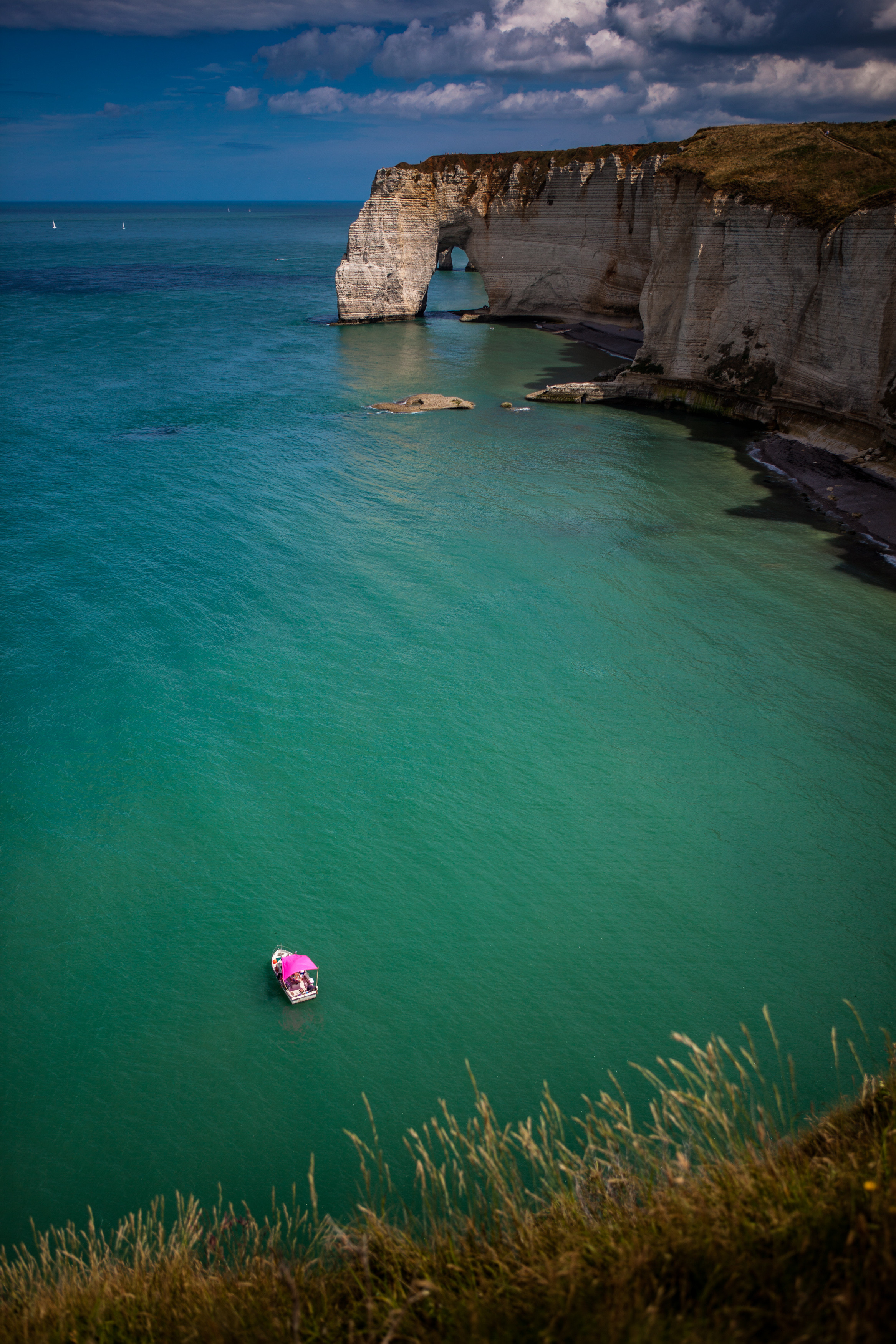 Coastal cliffs with a natural arch formation over turquoise waters, with a pink-roofed boat floating near the shore. Coastal cliffs with a natural arch formation over turquoise waters, with a pink-roofed boat floating near the shore.