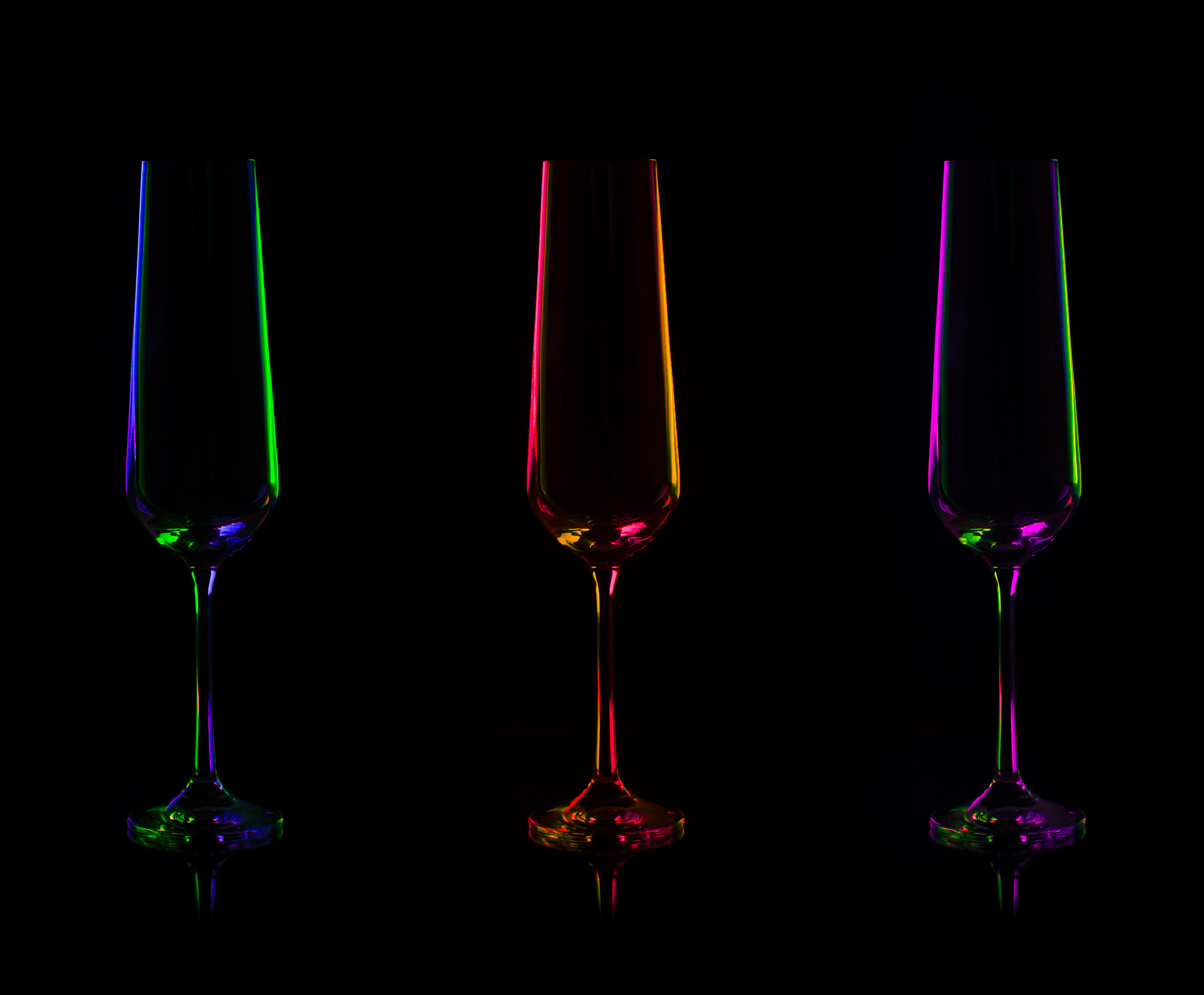 Three champagne glasses with colorful neon glow along the edges on a dark background. Three champagne glasses with colorful neon glow along the edges on a dark background.