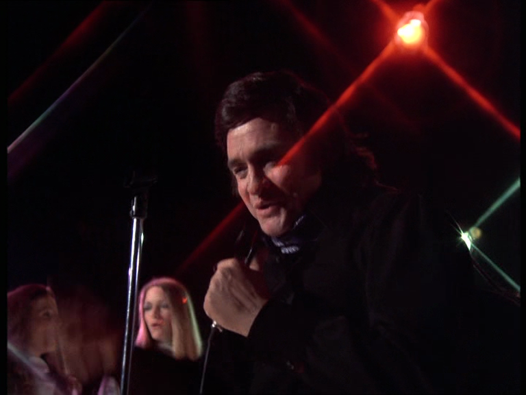 Johnny Cash tout sourire chante sur scène sous la lumière des spotlights Johnny Cash tout sourire chante sur scène sous la lumière des spotlights