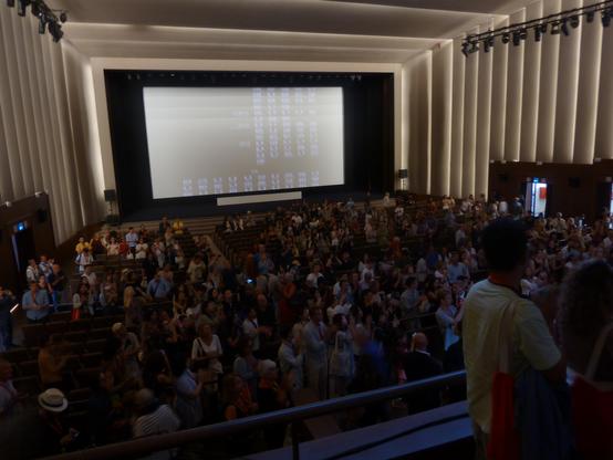 Standing ovation at the end of the projection. The audience is turned back towards the actors and crew, clapping.