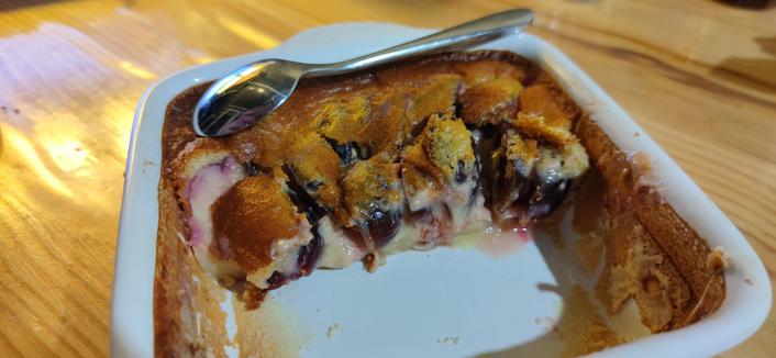Moitié de clafoutis avec des morceaux de fruits visibles dans un plat. Une cuillère est posée dessus.