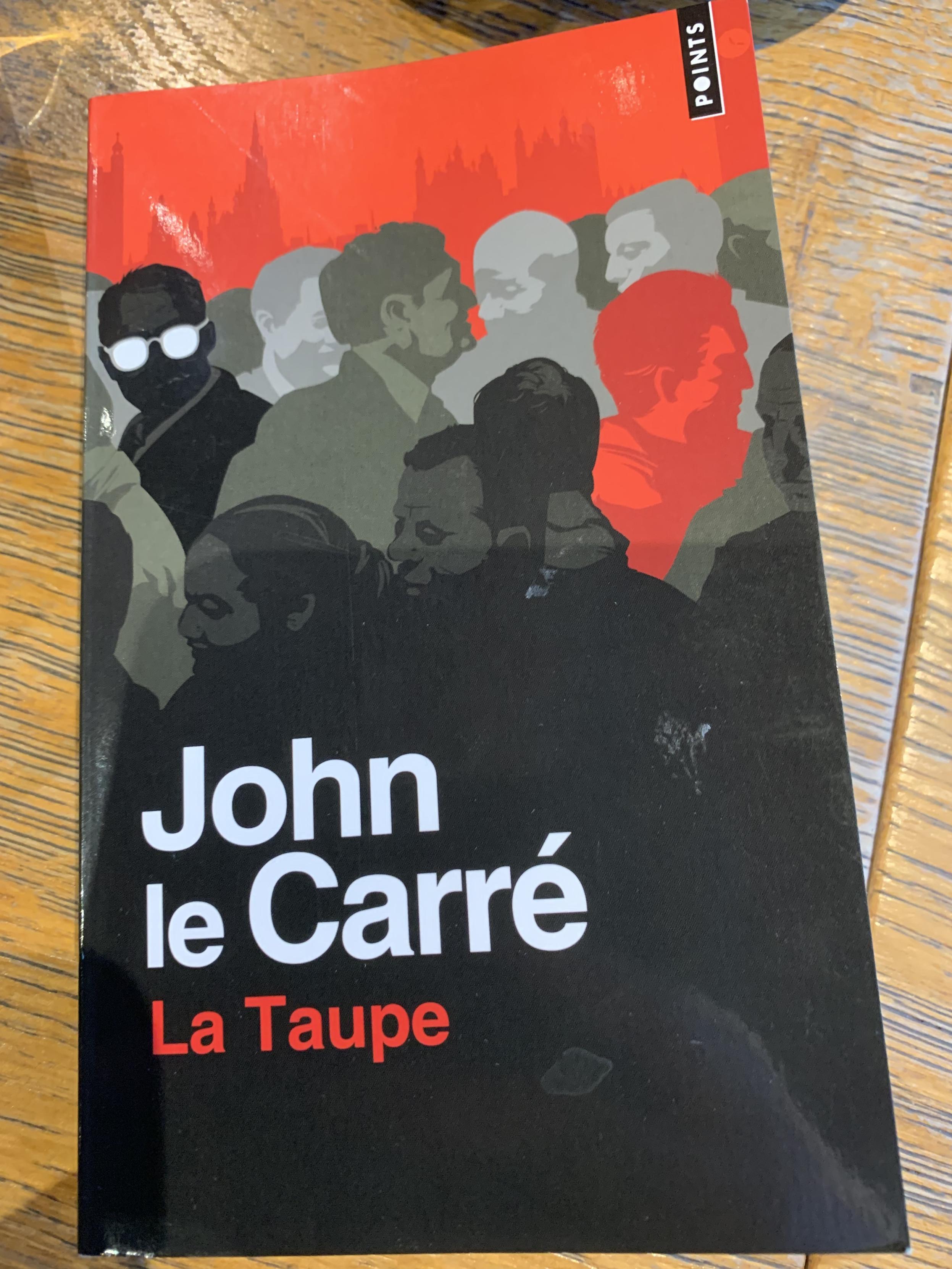 Couverture graphique stylée du roman "la Taupe" de John La Carré. Aplats noirs, ruges, gris. Evoque une surveillance dans la foule, un monde parallèle, à part.