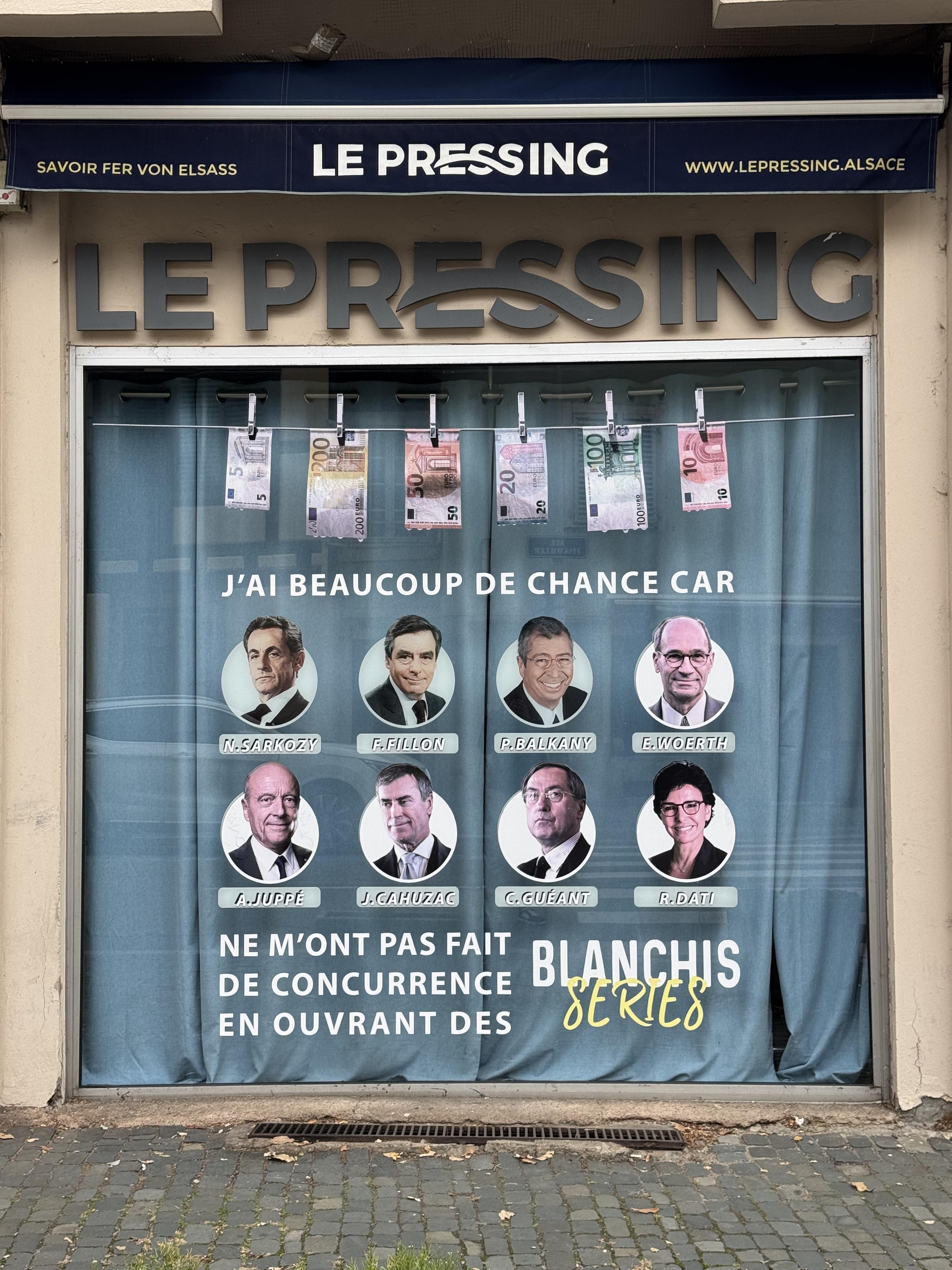 Photo d’une devanture de pressing. Des billets sèchent sur une corde à linge. Il y a des portraits de personnes politiques de droite.
Il est écrit : « j’ai beaucoup de chances car ils ne m’ont pas fait concurrence en ouvrant des blanchisseries »