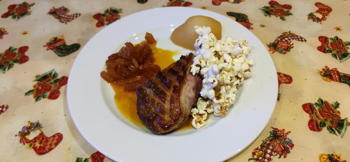 magret de canard, oranges confites, poire pochée, pop cornes dans une assiette blanche posée sur une nappe de Noël.
