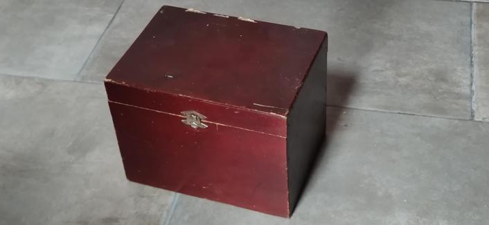 une boîte rouge sur un carrelage gris. Elle est usée, elle est fermée.