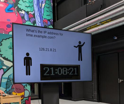 Screen in the Kraken Technology Centre showing a stick figure asking what's the IP address for time.example.com and another stick figure responds saying 126.21.8.21, and this maps to the timestamp 21:08:21.