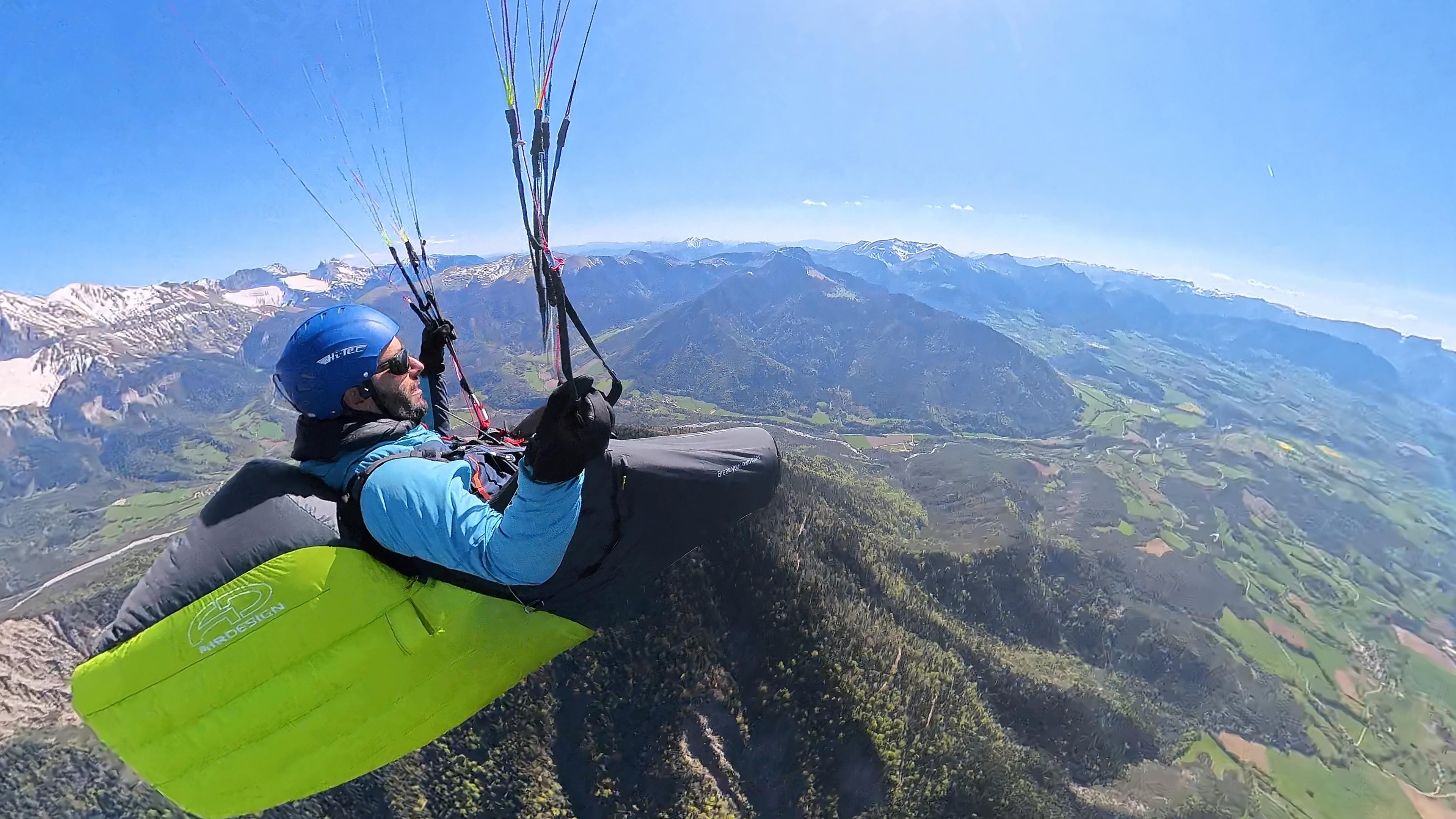 Parapentiste en altitude au dessus d'une colline couverte de forêt.