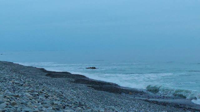 depuis la plage de galets de Pouldreuzic, après le coucher de soleil, le phare d'Eckmühl clignote au loin. mer calme.