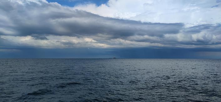 Mer d'Iroise sous une cellule orageuse. À l'horizon, perché sur un éperon rocheux, le phare de Tevennec, minuscule point blanc sur la photo. Le ciel fantastique et menaçant se reflète à la surface de l'eau, produisant des nuances de zones claires ou sombres.