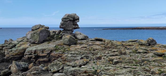 sur l'île de Sein, un rocher en forme de visage de style cubiste. Plus loin, mer calme et ciel bleu.