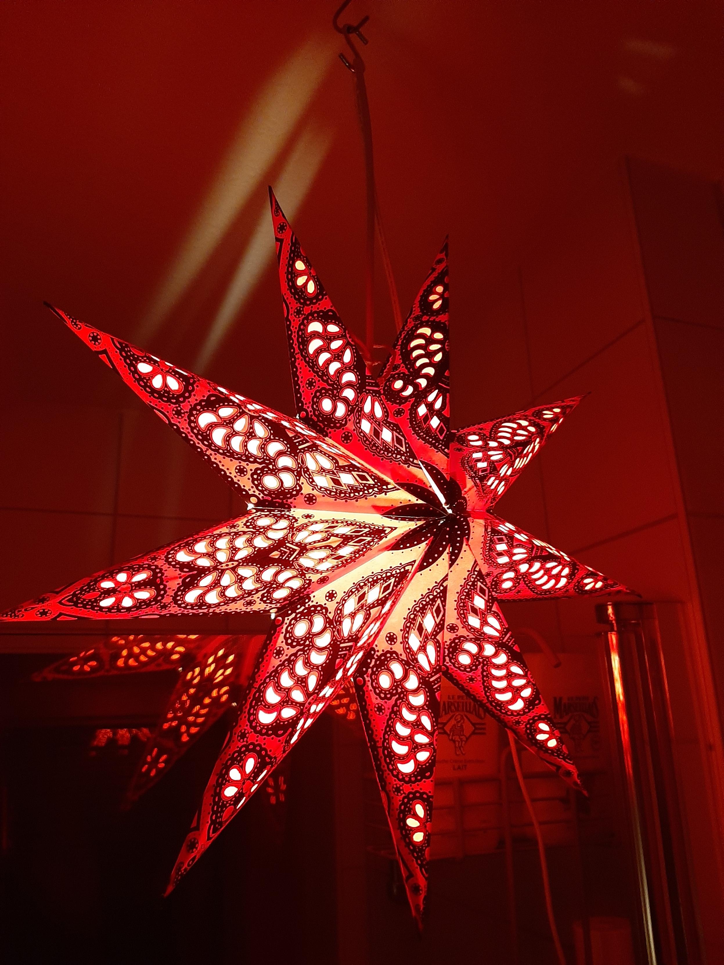 Décoration de Noël en forme d'étoiles ajourée pour laisser passer la lumière de l'ampoul à l'intérieur. L'étoile est rouge et renvoie cette couleur sur les murs autour