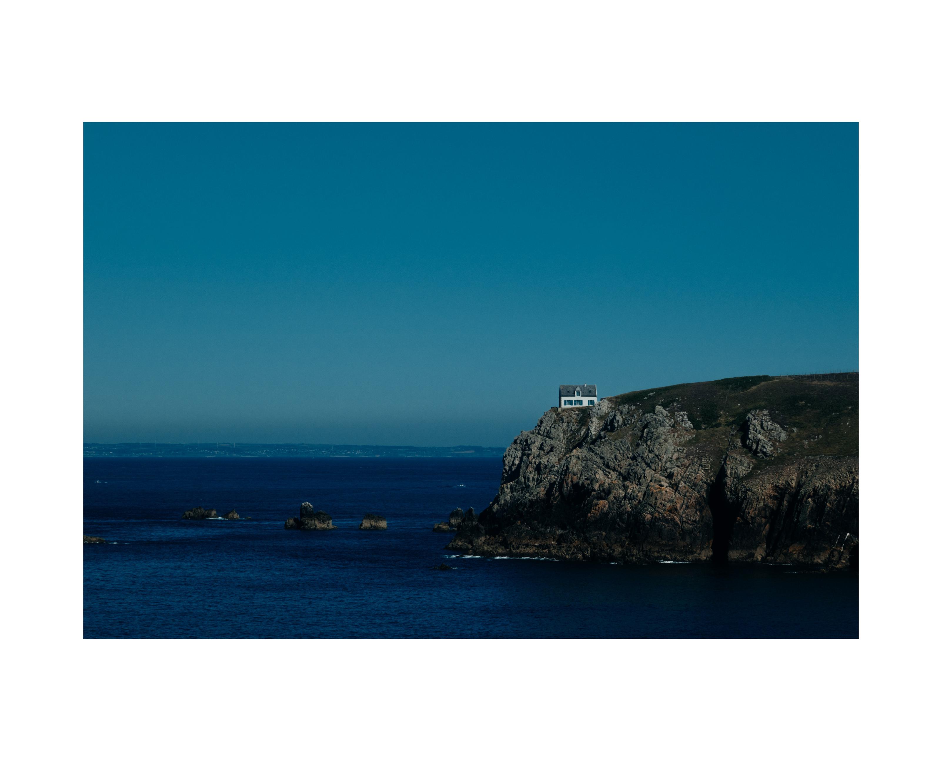 A white house at the edge of a cliff facing the sea