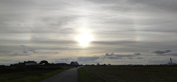dans un ciel chargé de voiles de nuages, le soleil à 30 degrés de l'horizon forme un parhélie (deux petites taches irisées en symétrie de part et d'autre du soleil). Phénomène dû à des cristaux de glace en altitude.