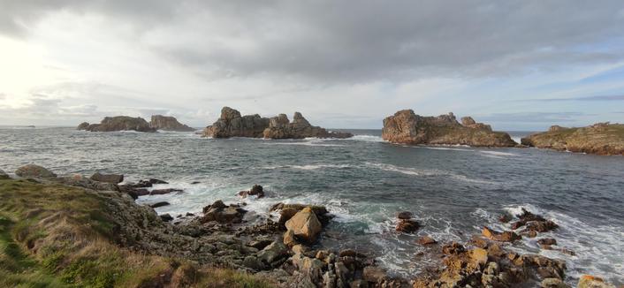 sous un ciel chargé de nuages mais lumineux, une enfilade de rochers au large protège l'entrée de la baie de yusin. de l'écume sur les rochers côtiers au premier plan